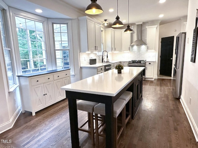 kitchen featuring wall chimney exhaust hood, appliances with stainless steel finishes, a sink, dark wood finished floors, and baseboards