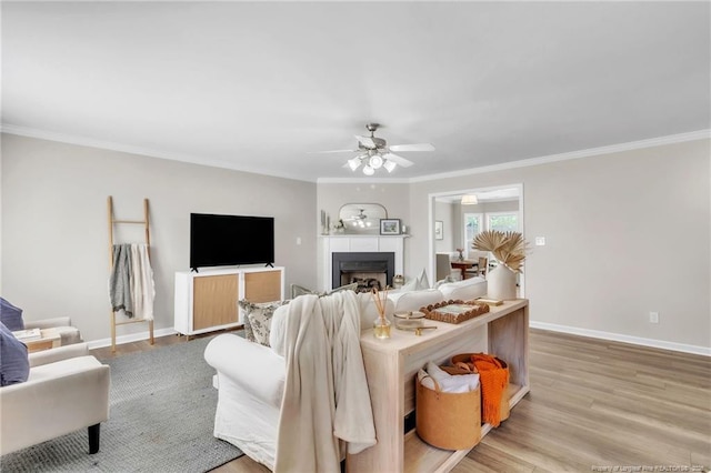 living room featuring ornamental molding, wood finished floors, a ceiling fan, baseboards, and a fireplace