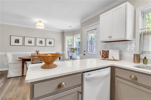 kitchen featuring dishwasher, a peninsula, light wood-type flooring, light stone countertops, and ornamental molding