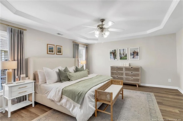 bedroom with a tray ceiling, wood finished floors, baseboards, and ceiling fan