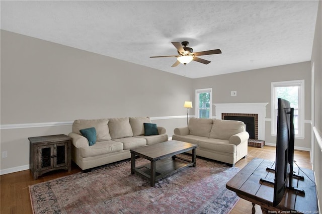 living area with wood finished floors, ceiling fan, a fireplace, baseboards, and a textured ceiling