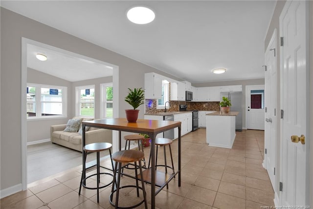 kitchen featuring stainless steel appliances, a sink, light tile patterned floors, open floor plan, and white cabinets