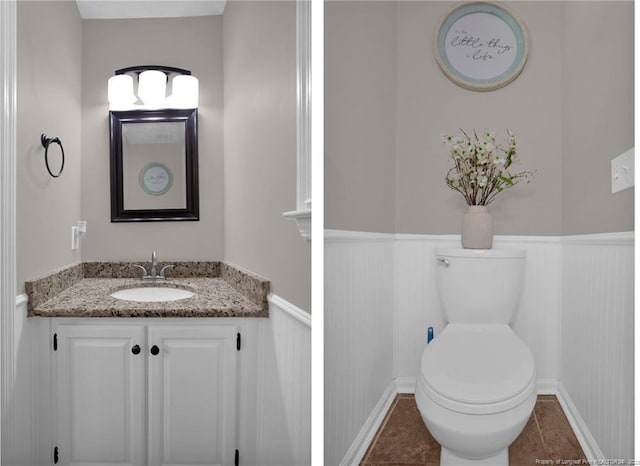 half bath featuring toilet, wainscoting, vanity, and tile patterned flooring