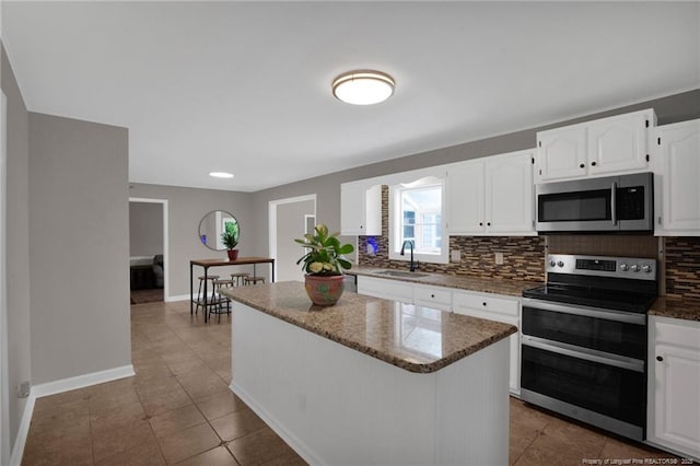kitchen featuring appliances with stainless steel finishes, backsplash, a sink, dark stone counters, and a kitchen island