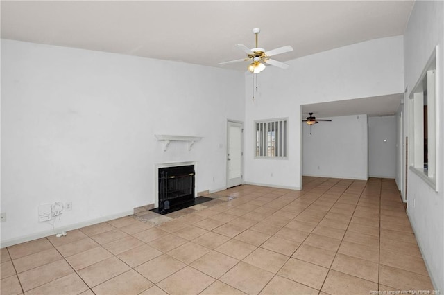 unfurnished living room with ceiling fan, light tile patterned floors, a fireplace, and a high ceiling