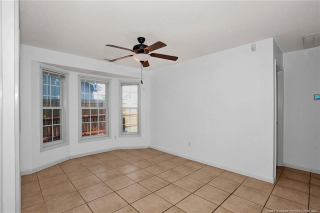 empty room featuring a ceiling fan, light tile patterned flooring, baseboards, and a textured ceiling