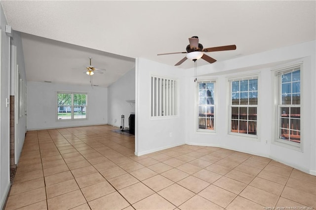 empty room with ceiling fan, light tile patterned flooring, a fireplace, lofted ceiling, and baseboards