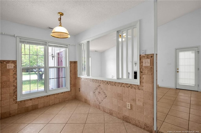 unfurnished dining area with tile walls, tile patterned flooring, plenty of natural light, a textured ceiling, and a wainscoted wall