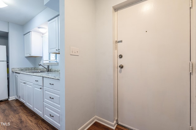 kitchen with a sink, white appliances, dark wood finished floors, white cabinetry, and baseboards