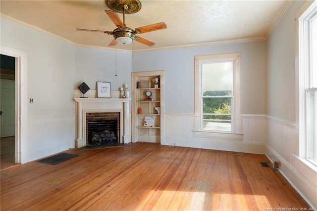 5648 Tolarsville Rd, Saint Pauls, NC 28384 - unfurnished living room featuring light wood-type flooring, a wainscoted wall, a ceiling fan, a fireplace with flush hearth, and crown molding