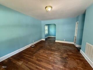 empty room with wood finished floors, arched walkways, and baseboards