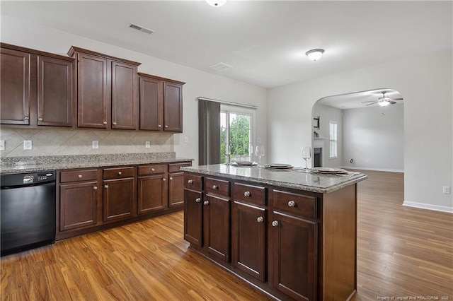 kitchen with dishwashing machine, light wood-style flooring, arched walkways, light stone countertops, and decorative backsplash