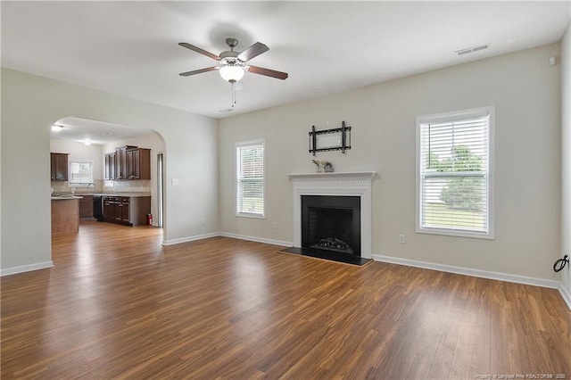 unfurnished living room featuring a ceiling fan, healthy amount of natural light, dark wood finished floors, and baseboards