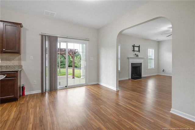 unfurnished living room with wood finished floors, arched walkways, and baseboards