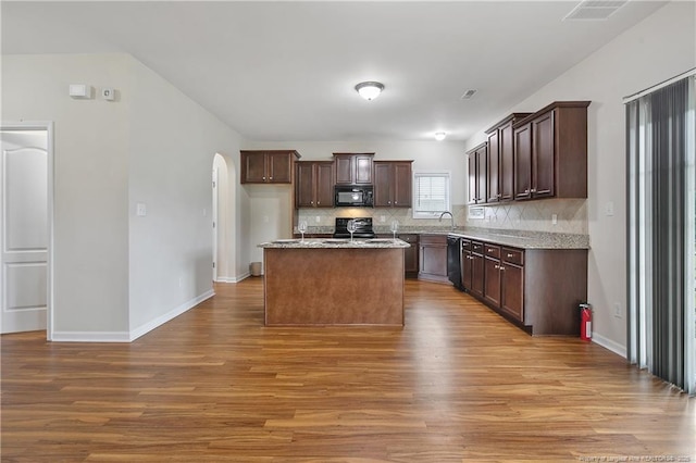 kitchen with black appliances, wood finished floors, decorative backsplash, and arched walkways