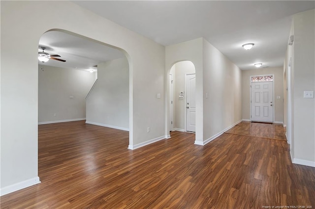 unfurnished room featuring a ceiling fan, arched walkways, wood finished floors, and baseboards