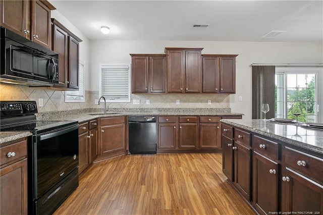 kitchen featuring black appliances, a sink, light wood finished floors, light stone counters, and tasteful backsplash