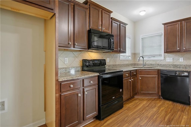 kitchen with black appliances, a sink, light wood-style flooring, backsplash, and light stone counters