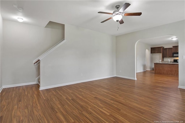 unfurnished living room with a ceiling fan, arched walkways, and dark wood-style flooring