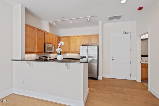 317 W Morgan St Unit 320, Raleigh, NC 27601 - kitchen with appliances with stainless steel finishes, dark countertops, a peninsula, a kitchen bar, and light wood-style floors