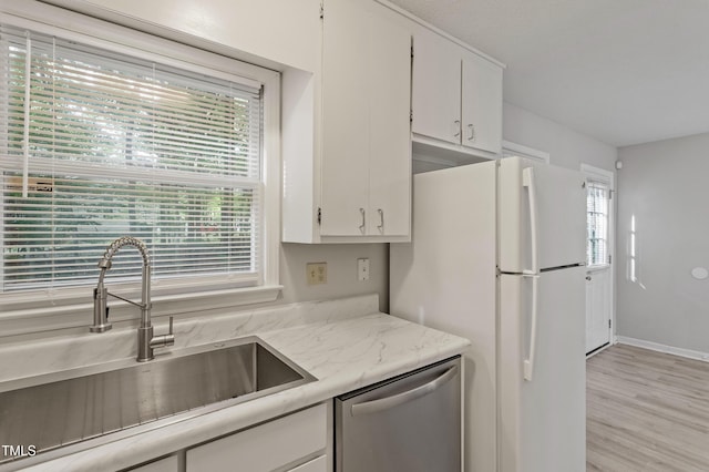 kitchen with dishwasher, a sink, freestanding refrigerator, white cabinetry, and light wood finished floors