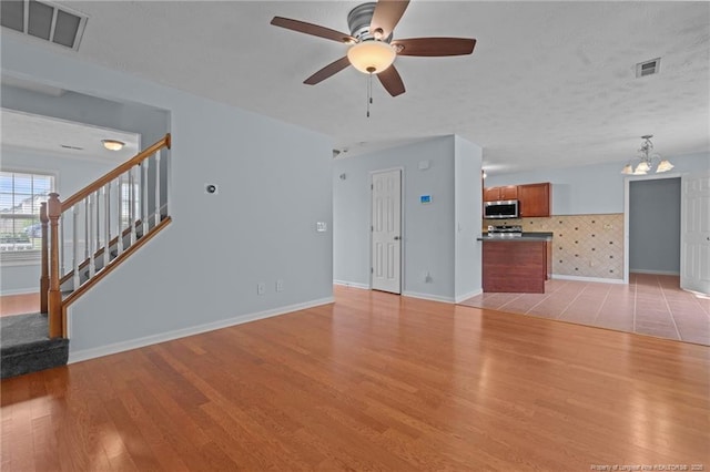 11 Checkmate Ct, Cameron, NC 28326 - unfurnished living room with light wood-type flooring, ceiling fan, baseboards, stairs, and a chandelier