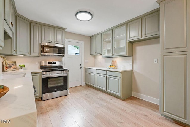 847 E Maple Ln, Fuquay Varina, NC 27526 - kitchen with appliances with stainless steel finishes, gray cabinets, a sink, light wood-type flooring, and glass insert cabinets