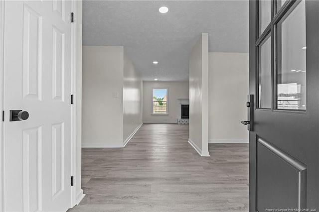 entryway featuring light wood-type flooring, baseboards, a textured ceiling, a fireplace with raised hearth, and recessed lighting