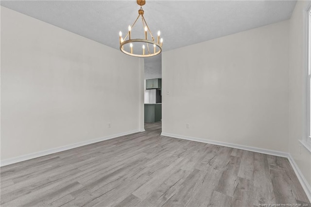 empty room featuring a chandelier, wood finished floors, and baseboards