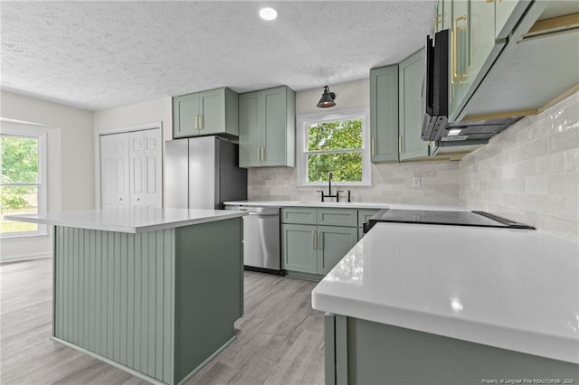 kitchen with appliances with stainless steel finishes, green cabinetry, light wood-style floors, tasteful backsplash, and a textured ceiling