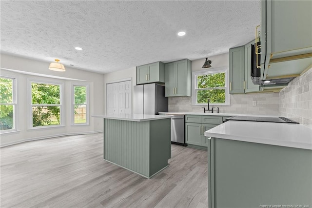 kitchen featuring green cabinets, appliances with stainless steel finishes, a textured ceiling, light wood finished floors, and tasteful backsplash