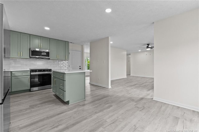 kitchen featuring stainless steel appliances, green cabinetry, ceiling fan, light countertops, and a center island