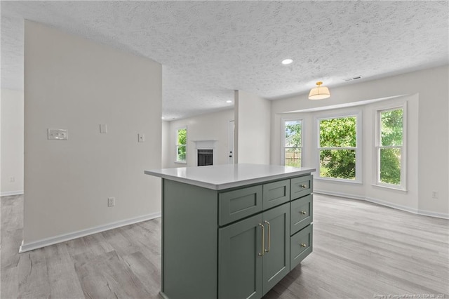 kitchen with green cabinetry, light wood-style flooring, a textured ceiling, light countertops, and a center island