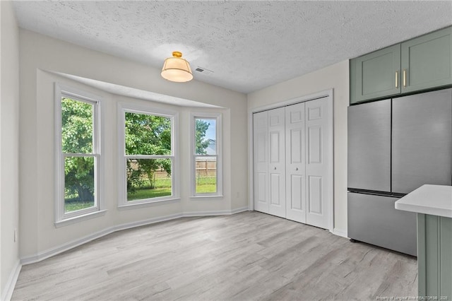 unfurnished bedroom featuring freestanding refrigerator, light wood finished floors, baseboards, and a textured ceiling
