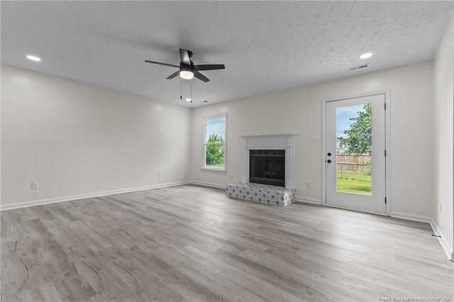 unfurnished living room with a ceiling fan, wood finished floors, baseboards, a fireplace with raised hearth, and a textured ceiling