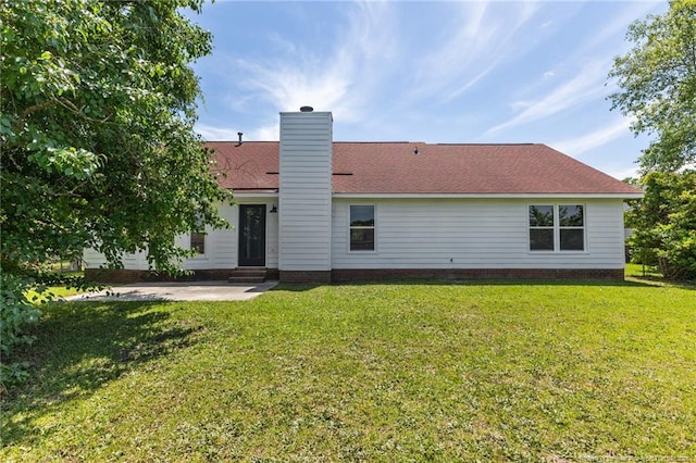 back of house featuring a lawn, a patio area, a chimney, and a shingled roof