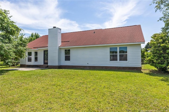 back of property featuring a lawn, a chimney, a patio area, and a shingled roof
