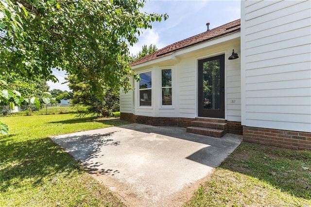 view of exterior entry featuring a lawn and a patio