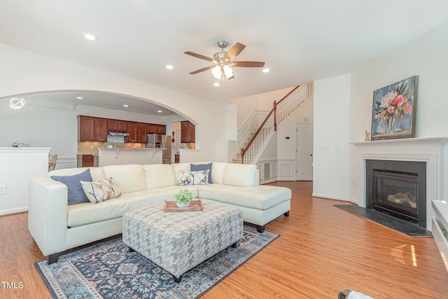 233 Hammond Wood Pl, Morrisville, NC 27560 - living area featuring arched walkways, a ceiling fan, light wood-style floors, stairs, and a fireplace with flush hearth
