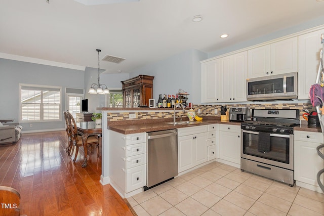 8004 Thrush Ridge Ln, Raleigh, NC 27615 - kitchen with appliances with stainless steel finishes, dark countertops, a peninsula, a chandelier, and decorative backsplash