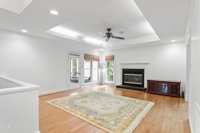 108 Ripplewater Ln, Cary, NC 27518 - living room featuring a raised ceiling, a ceiling fan, light wood-style floors, a glass covered fireplace, and ornamental molding