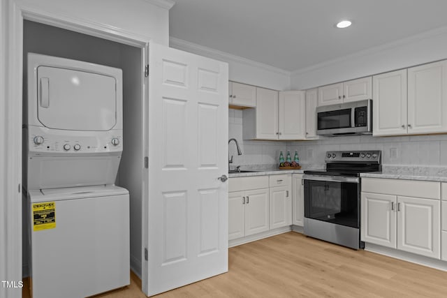 1204 Pecan Pl, Durham, NC 27704 - kitchen with appliances with stainless steel finishes, stacked washing machine and dryer, ornamental molding, a sink, and white cabinets