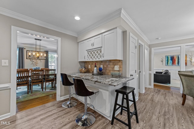 2901 Ceremonial Ct, Raleigh, NC 27615 - kitchen with light wood finished floors, light stone counters, a kitchen bar, backsplash, and ornamental molding