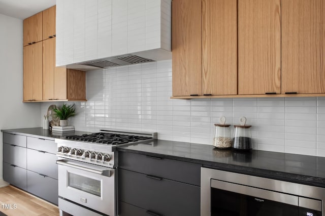 1405 Watts St, Durham, NC 27701 - kitchen featuring appliances with stainless steel finishes, wall chimney range hood, backsplash, and light wood-style flooring