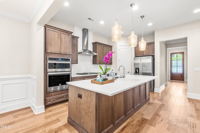 192 Glenpark Pl, Cary, NC 27511 - kitchen with wall chimney exhaust hood, stainless steel appliances, a kitchen island with sink, light wood finished floors, and recessed lighting
