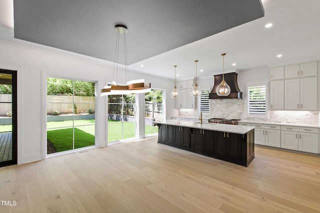 2805 Van Dyke Ave, Raleigh, NC 27607 - kitchen featuring premium range hood, light countertops, backsplash, light wood-style flooring, and white cabinetry