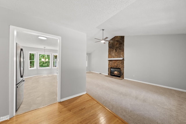 6009 Shadow Moss Cir, Raleigh, NC 27603 - unfurnished living room featuring a ceiling fan, light wood-style flooring, a stone fireplace, vaulted ceiling, and baseboards