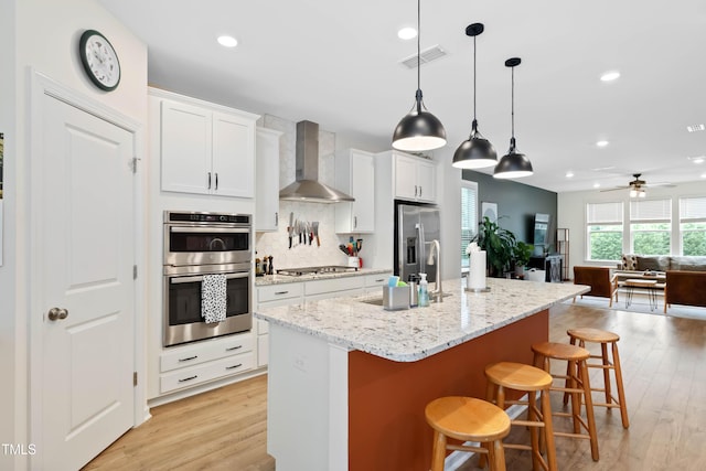 6928 Leesville Rd, Raleigh, NC 27613 - kitchen featuring wall chimney exhaust hood, stainless steel appliances, open floor plan, light wood-style floors, and a breakfast bar