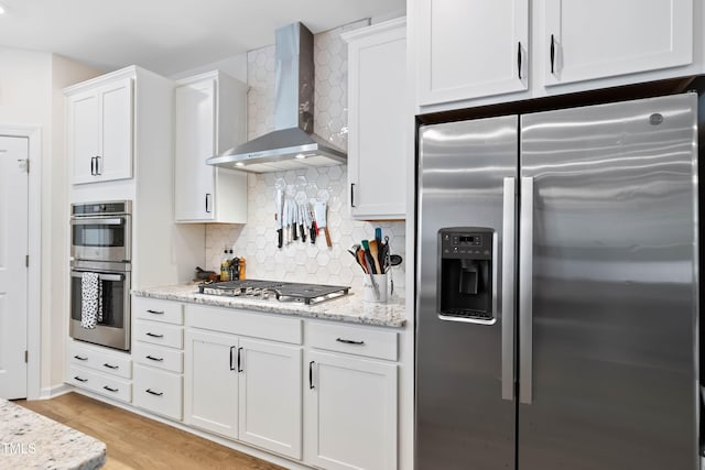 6928 Leesville Rd, Raleigh, NC 27613 - kitchen featuring appliances with stainless steel finishes, wall chimney range hood, white cabinetry, tasteful backsplash, and light stone countertops