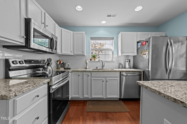 34 Tannenbaum Cir, Greensboro, NC 27410 - kitchen with appliances with stainless steel finishes, a sink, decorative backsplash, dark wood-type flooring, and light stone counters
